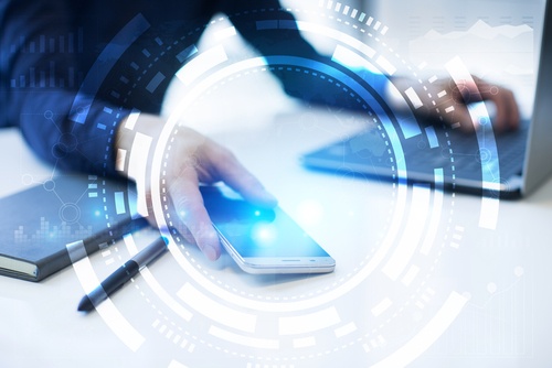 A person holding a cell phone with one hand and their other hand is on a laptop keyboard.